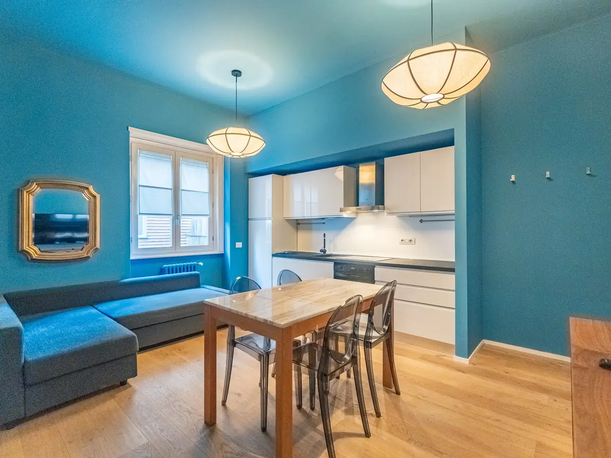 Blue living room with a grey sofa, wooden table and white open kitchen