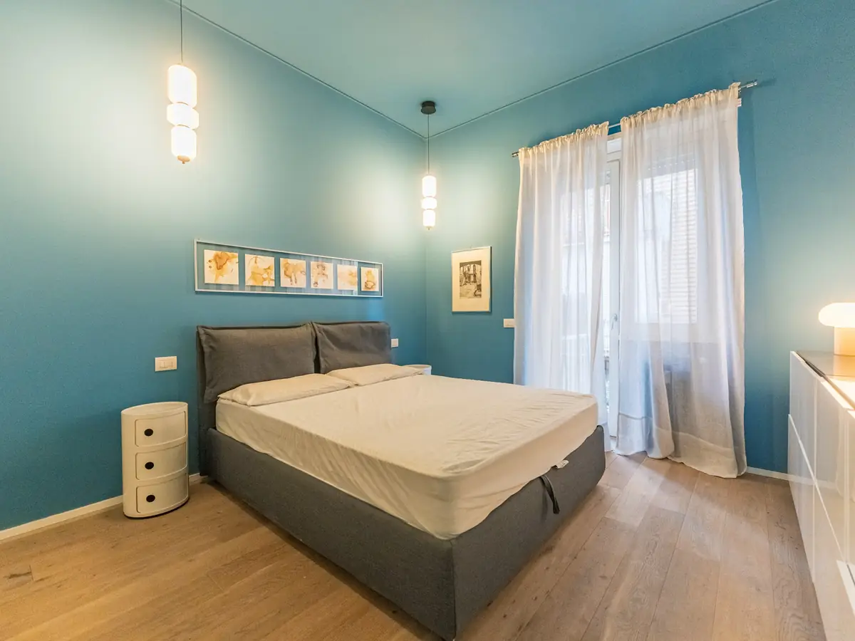 Blue bedroom with a double bed and a French window with white curtains